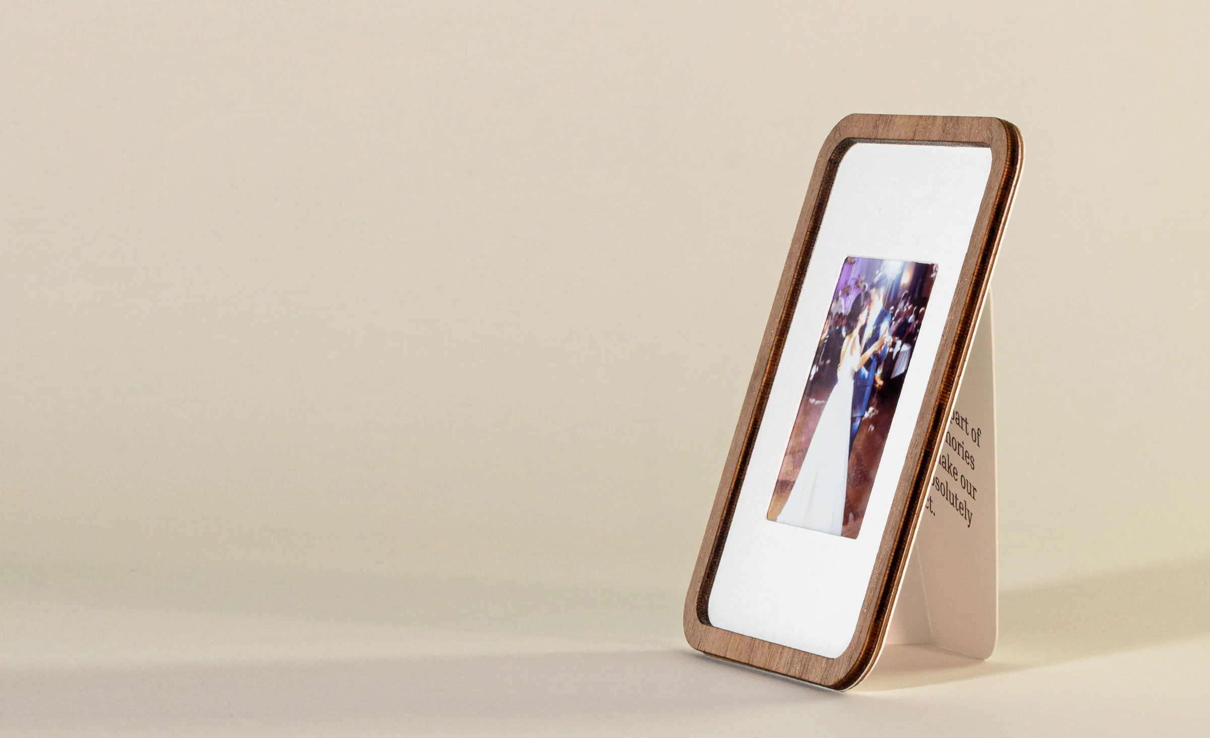 A walnut Pop-up Frame holding an instax mini wedding photo, standing on its card against a warm beige backdrop