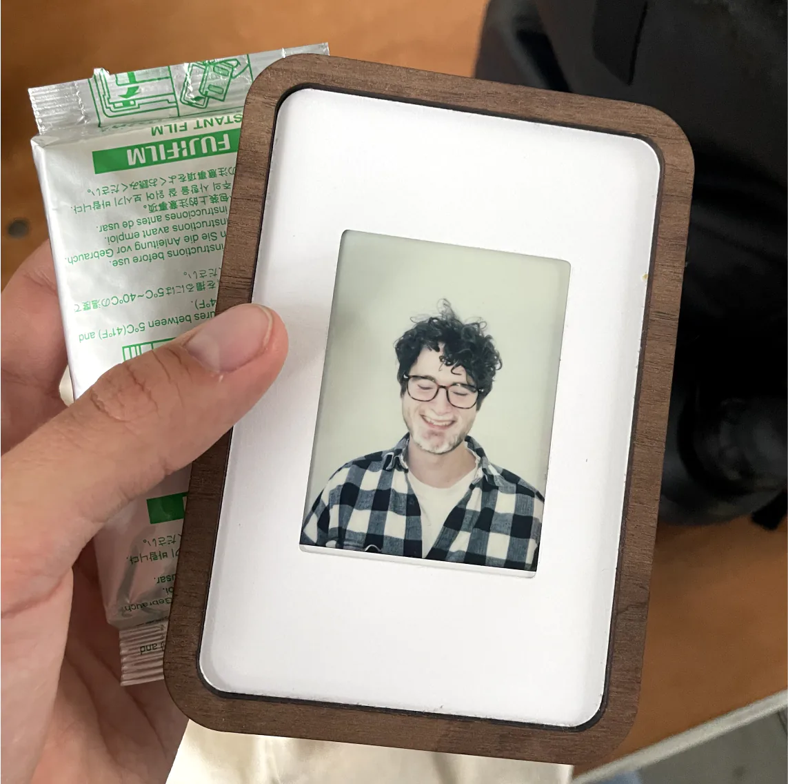 Hand holding a Pop-up Frame with an instant photo portrait, next to a pack of film